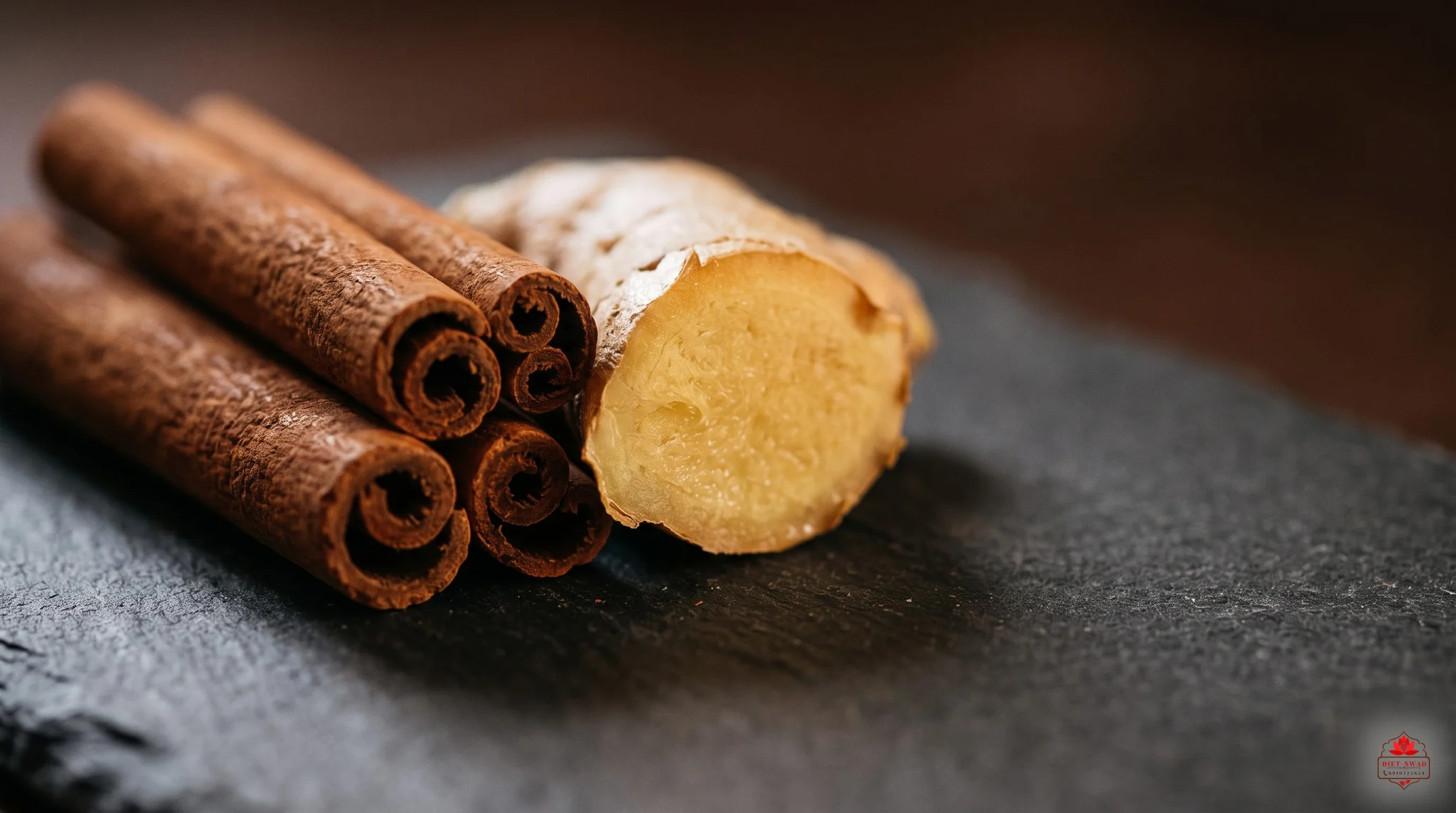 A close macro of cinnamon sticks beside a freshly cut piece of ginger on dark slate
