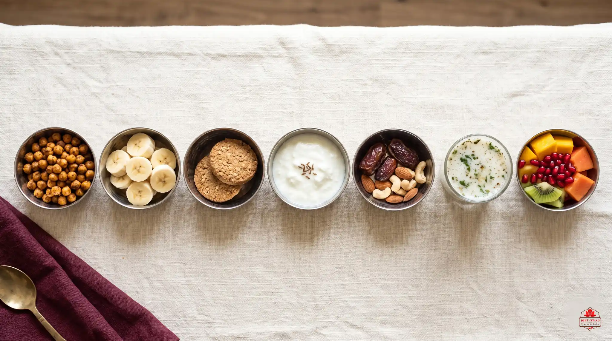 Seven small steel bowls in a row holding a week of snack swaps: roasted chana, banana, biscuits, curd, dates with nuts, buttermilk and cut fruit