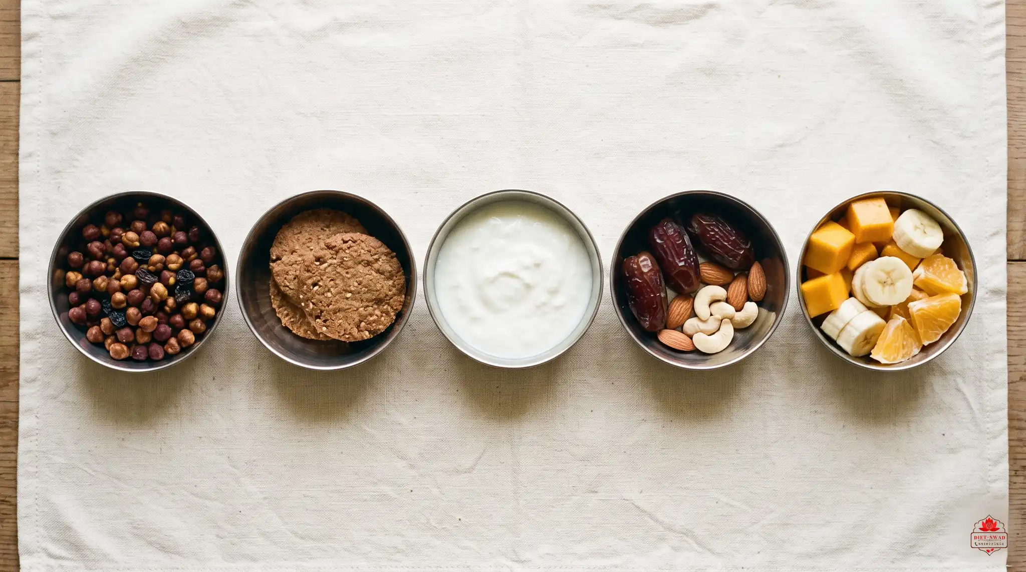 Five small steel bowls of everyday snacks: roasted chana with raisins, thin biscuits, curd, dates with nuts, and cut fruit
